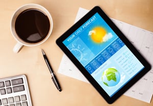 Workplace with tablet pc showing weather forecast and a cup of coffee on a wooden work table close-up